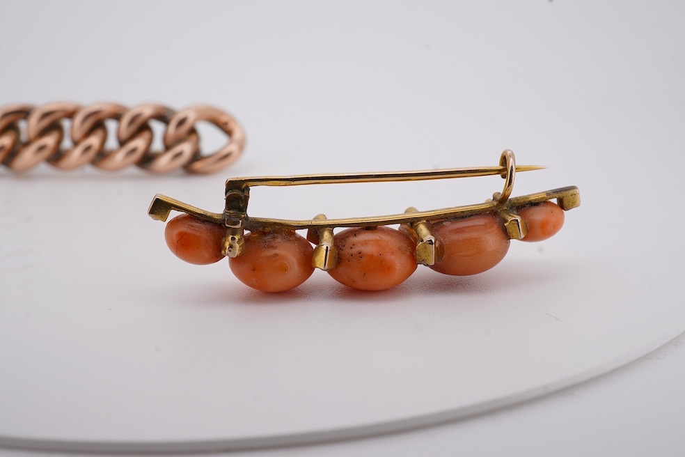 An early 20th century yellow metal and graduated five stone coral bead brooch, with seed pearl spacers, 45mm, together with a yellow metal curb link brooch and a yellow metal (stamped 9c) safety pin. Condition - fair